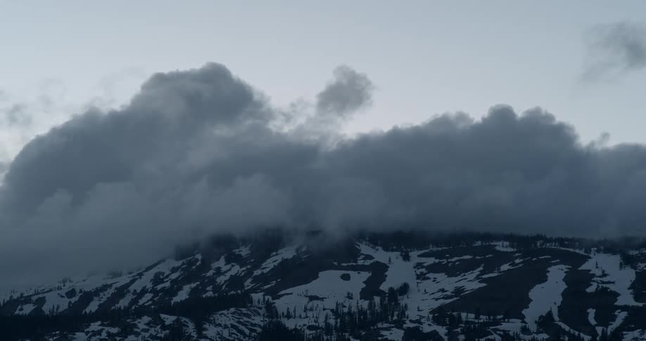 The clouds touch the top of the snow covered mountain