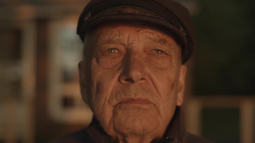 Older man wearing hat staring forward blinking