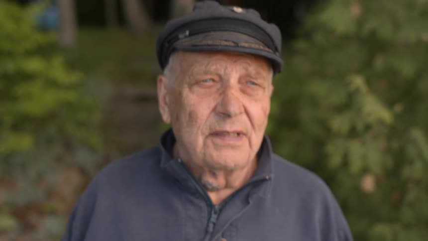 A very old white man walks down a path in a forest
