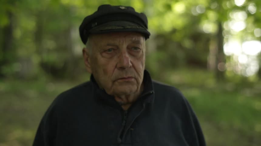 An older man wearing a black hat walking in a wooded area