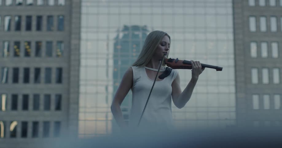 Woman stands in front of a tall building and plays the violin