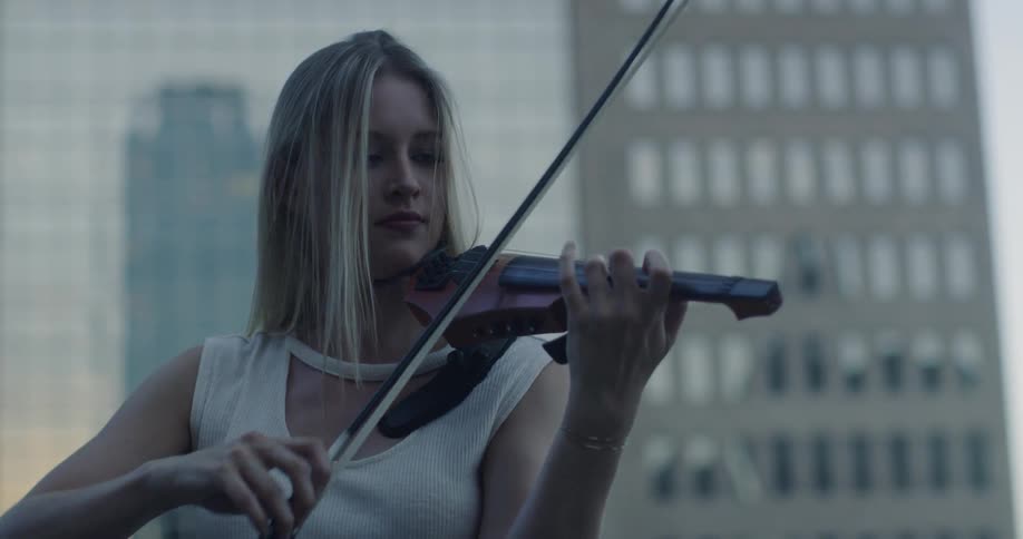 Woman stands in front of a tall building and plays the violin