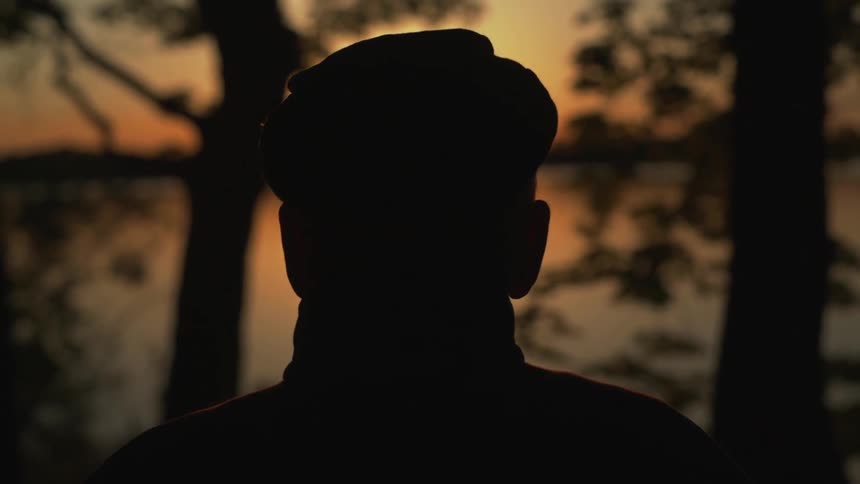 Man stands outside watching the water at sunset