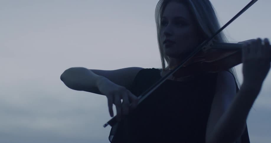 Woman is playing the violin outside on windy evening