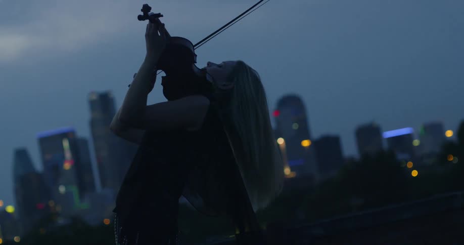 A woman plays a violin in the city at night