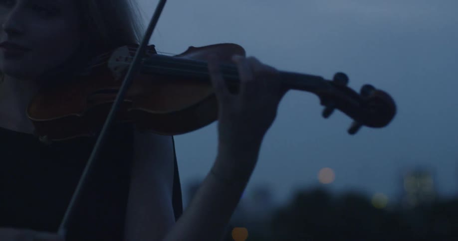Woman plays violin outside at dusk