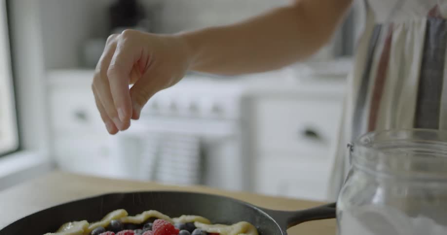 A woman sprinkles sugar on a berry pie before it is baked
