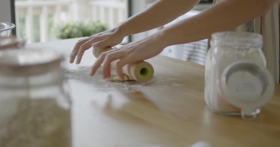 A woman adds flour to the dough before rolling it out