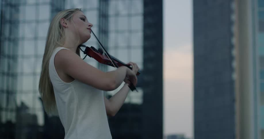 A woman is playing violin outside in a city at dusk