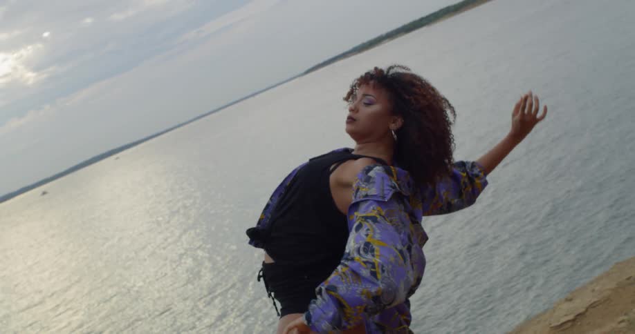 A woman dances abstractly next to a lake