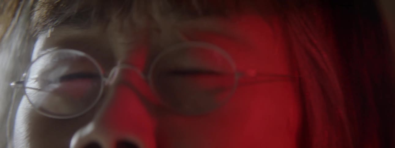 An asian woman wearing glasses clenches her eyes closed tightly