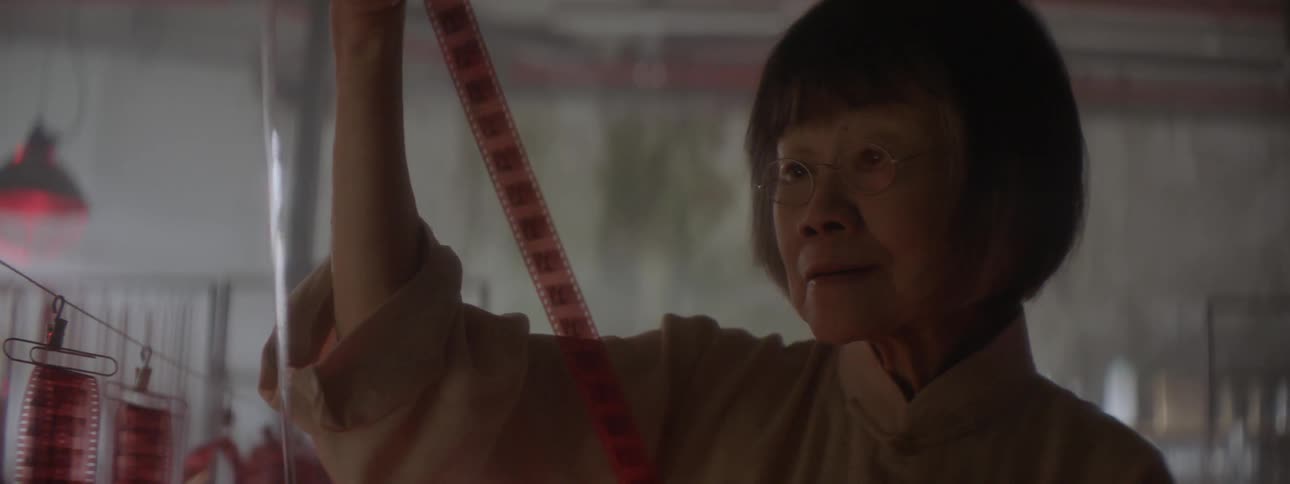An asian woman inspects a roll of film in a dark room