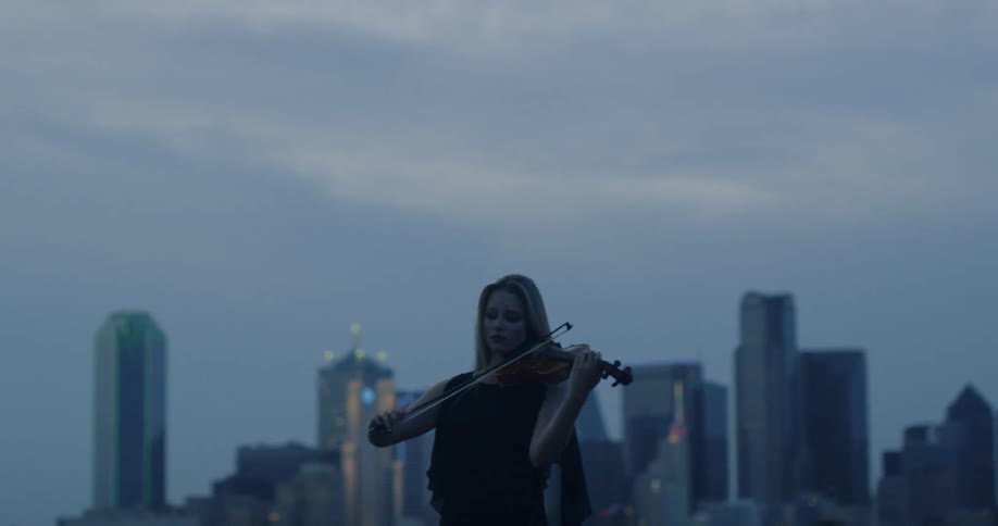 Woman plays violin with city skyscrapers in the distance