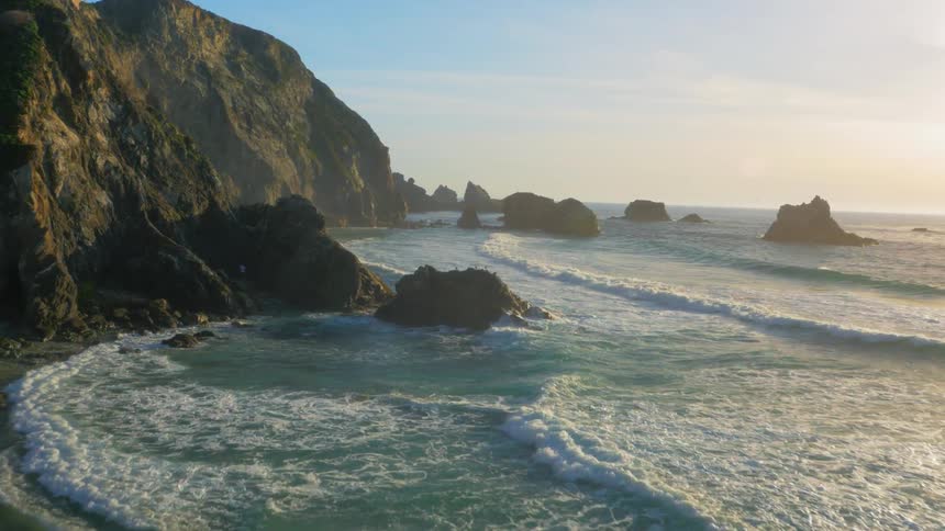 The waves slowly hit the shore and rocks on a sunny day