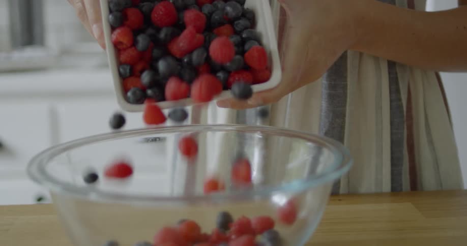 A woman pours berries into a glass mixing bowl