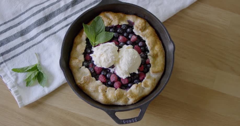 A berry pie topped with ice cream sits on a wood countertop