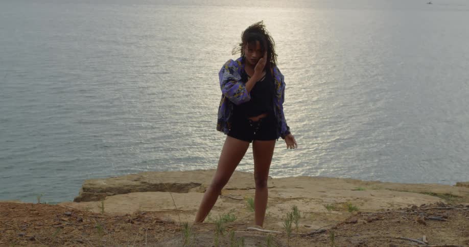 A woman dances next to a lake