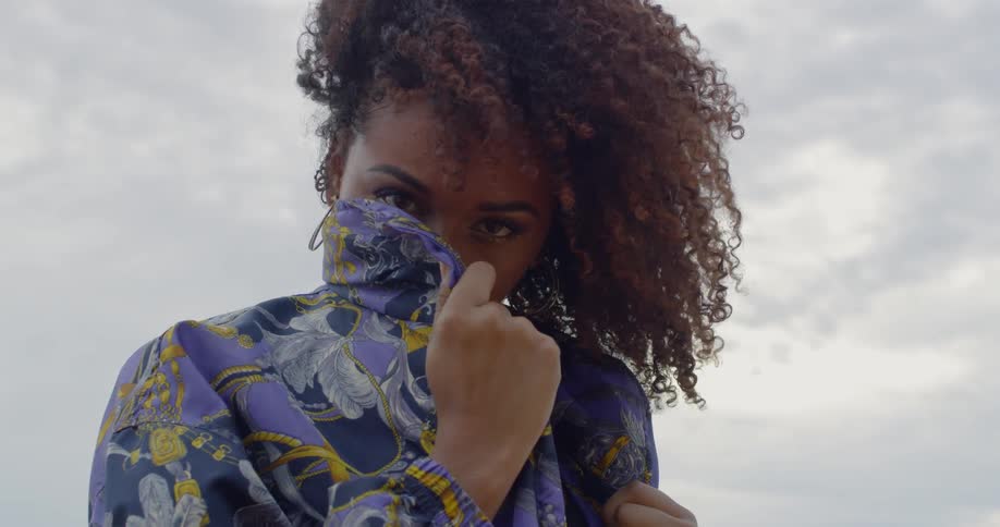 A woman hides her face with her jacket collar as the wind blows her hair