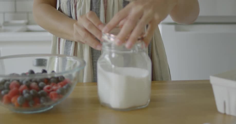 A woman grabs a canister of sugar and sprinkles some on a bowl of berries