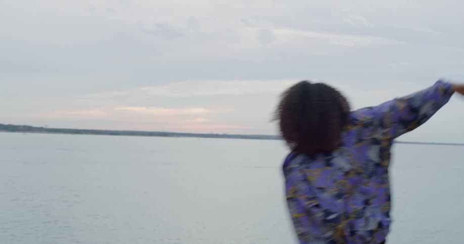 A woman dances next to a lake at sunset