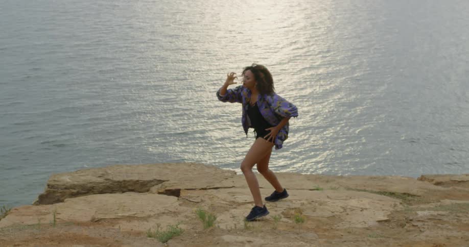 A woman dances by the edge of a cliff on a windy day