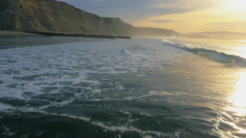 Ocean waves wash ashore a beach at sunset