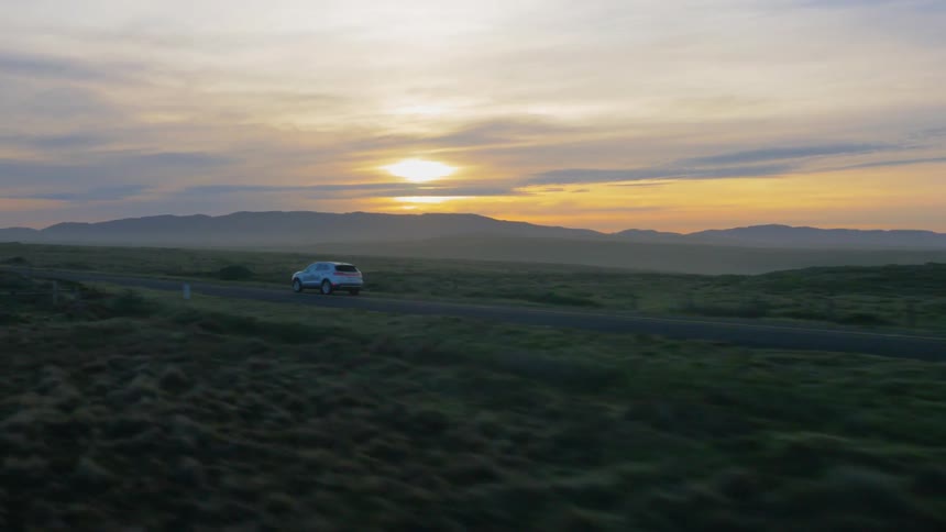 A vehicle travels down a rural road at dusk