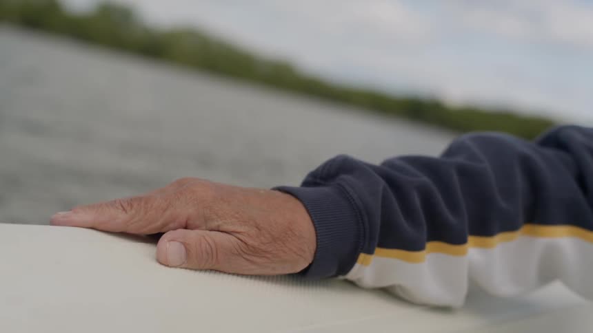 A shot of a man's hand resting on the side of a boat as it speeds through the water