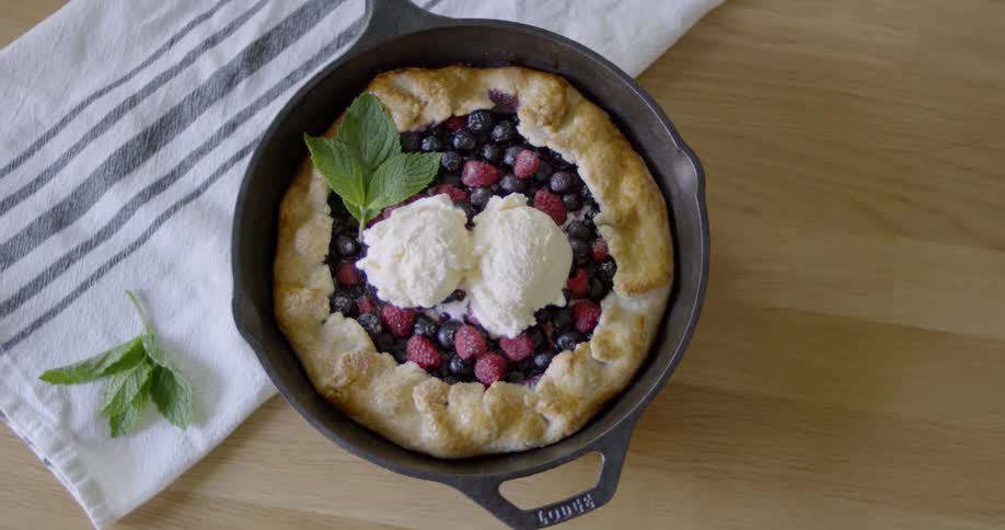 A berry pie topped with ice cream sits on a wood countertop