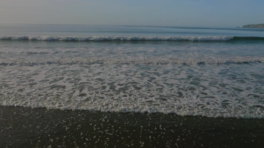 The waves crash against the sand on a sunny day