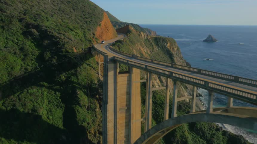 Cars traveling across tall bridge on the coast overlooking the ocean