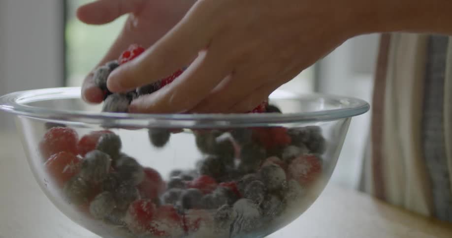 A person mixes some berries in a bowl