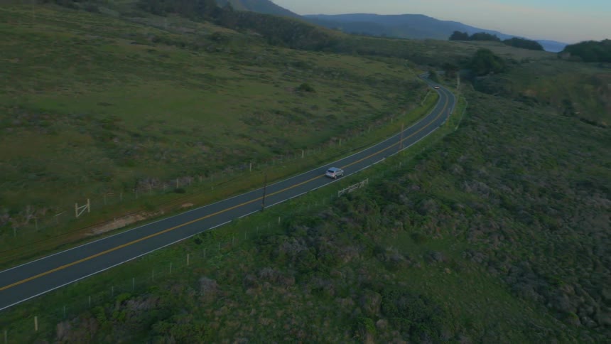 A car drives down the road surrounded by green
