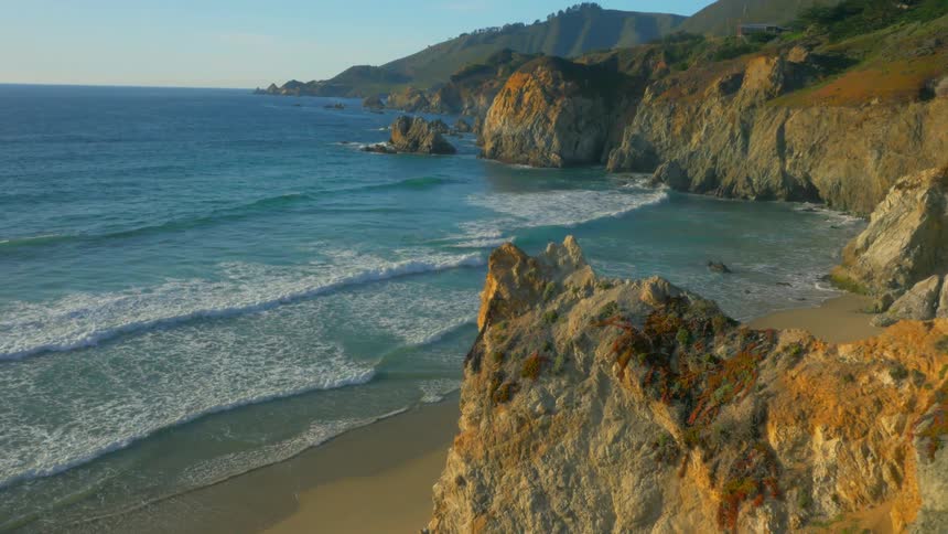 The waves crash against the shore by the cliffs of the beach