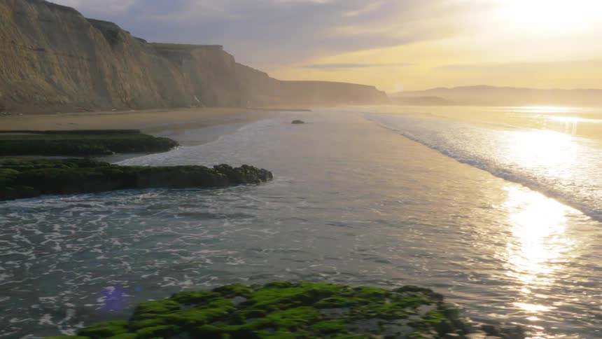 Cliffs line a beach as waves come to shore at sunset