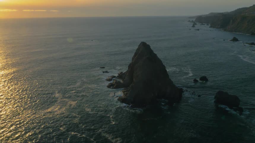 Ocean waves splash against the rocks at sunset