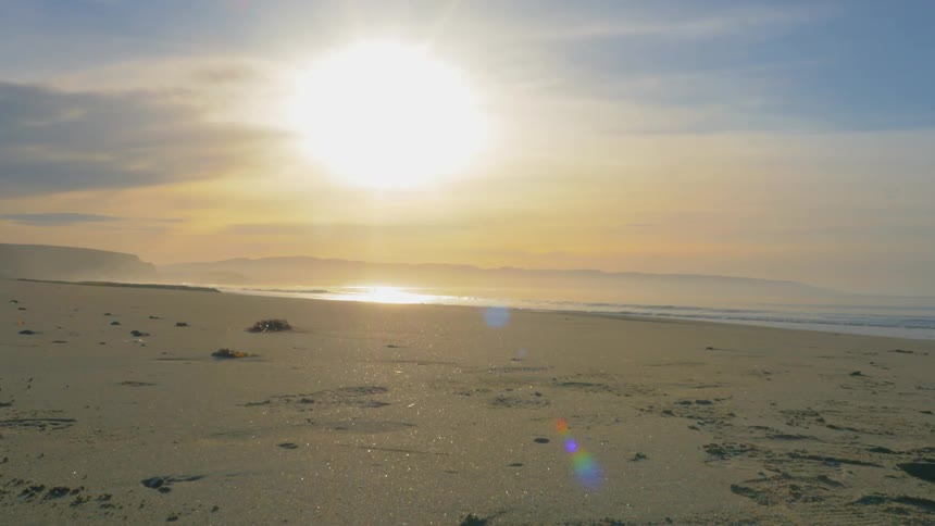 Sun rises over the ocean, shining light on the beach