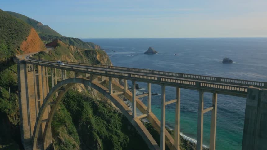 A vehicle drives over a tall bridge on the coast