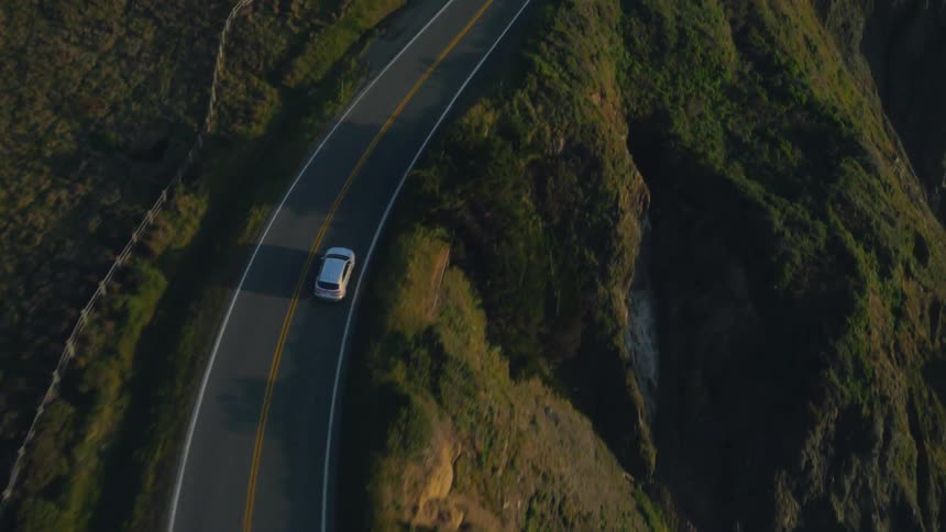 A vehicle travels down a coastal road by the ocean