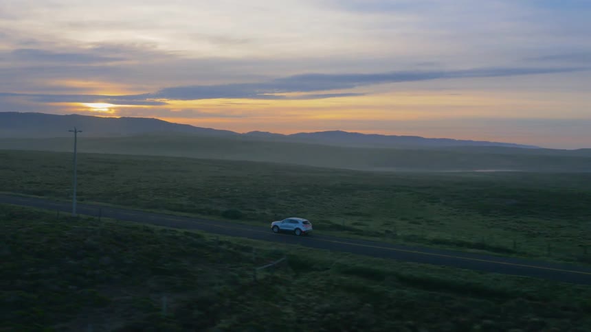 Vehicle driving along a barren road at a cloudy sunset
