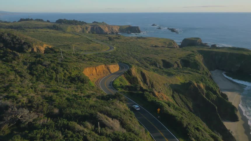 Car is driving on windy coastal road near ocean on sunny day