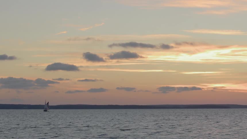 A sailboat sails on the ocean waters as the sun sets