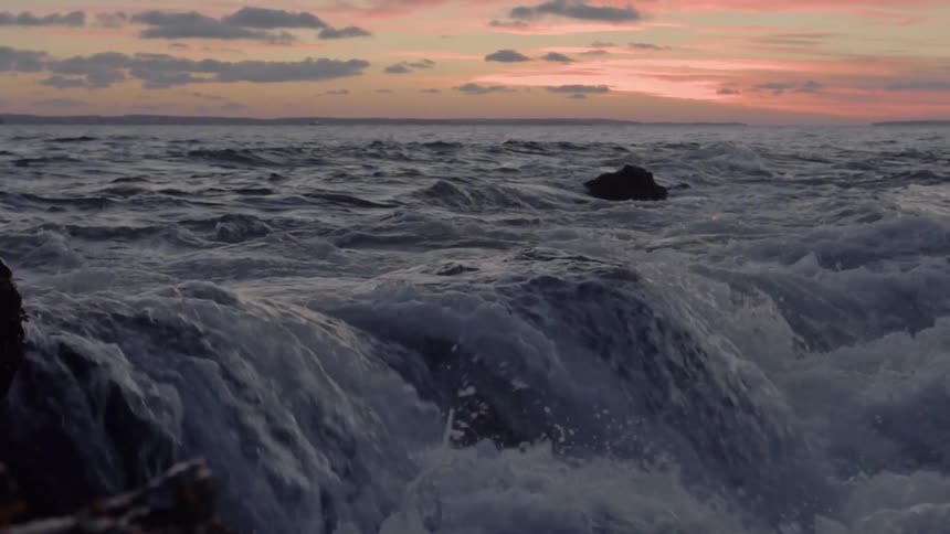 Ocean water crashing and splashing against rocks after sunset