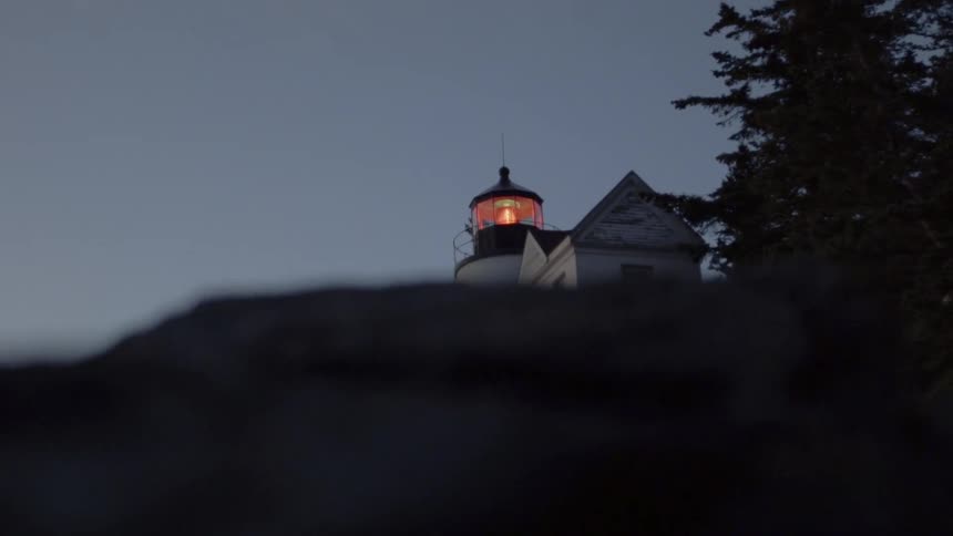 A Lighthouse Is Revealed Behind Rocks On The Beach