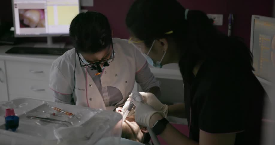 An assistant holds the suction hose as a dentist works on a patient