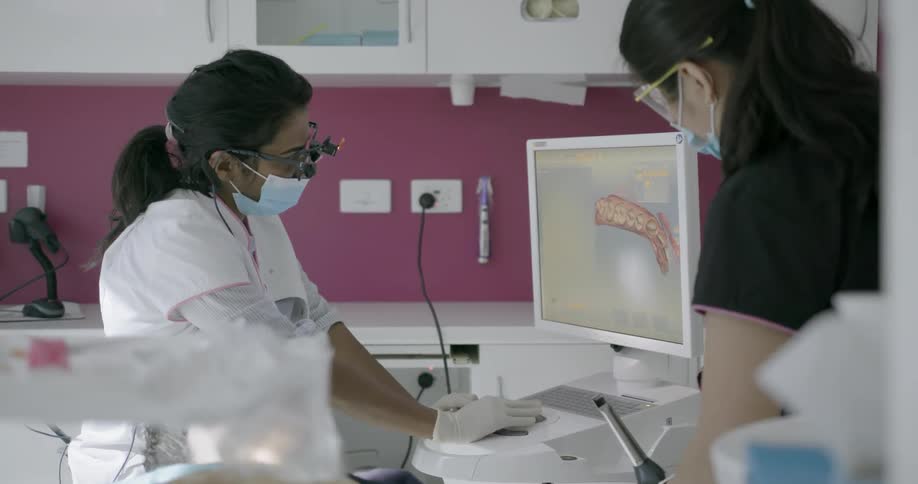 Two women work on a dental patient looking at a display