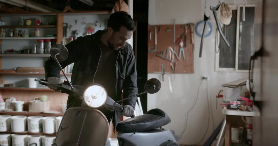 Man in garage turns on the light on parked scooter