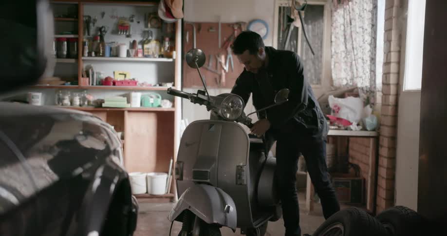 A man moves a scooter in a garage