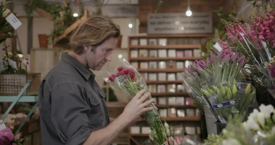 A man selects a bouquet of red flowers from a florist shop