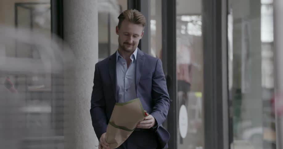 Man in suit walking on city sidewalk is carrying flower bouquet and smiling